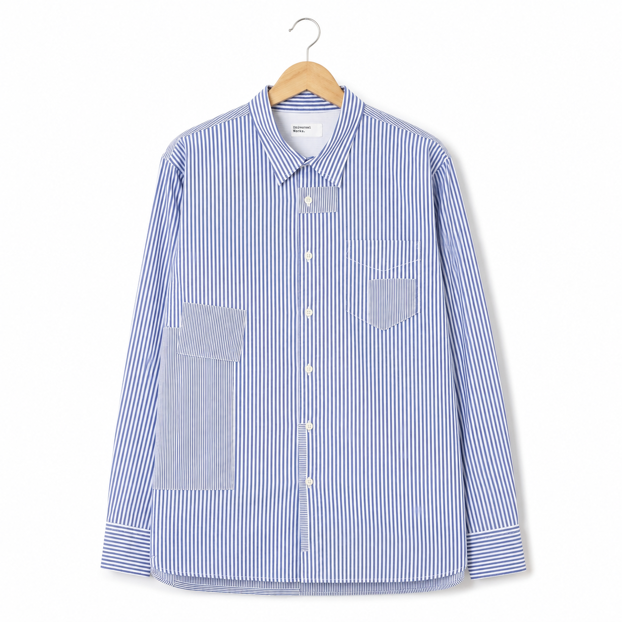 A long-sleeve button-up shirt with blue and white vertical stripes, featuring solid blue contrast pockets on the front, displayed on a wooden hanger against a clean white background.